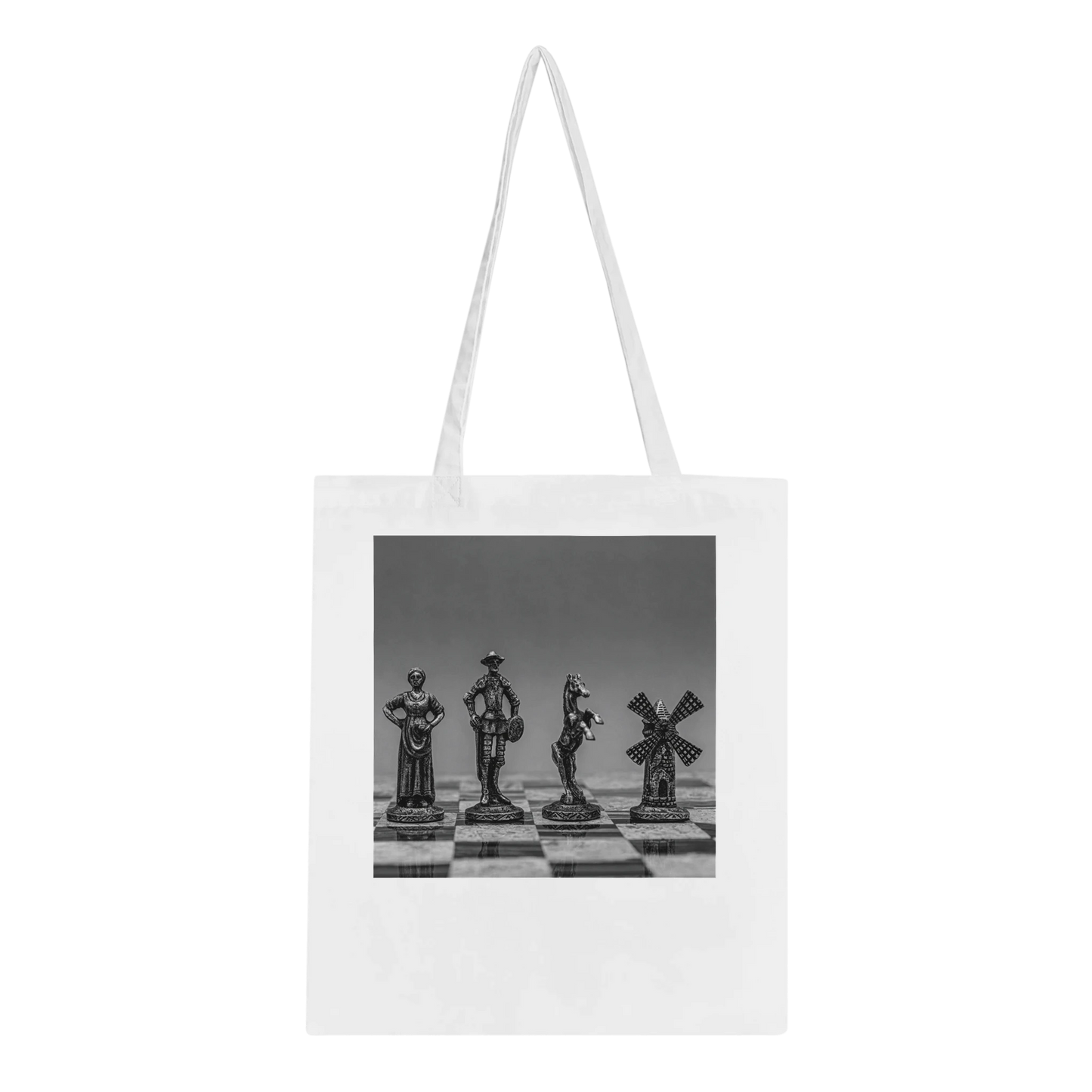 A white canvas tote bag with long shoulder straps, featuring a black and white photographic print of four chess pieces on a chessboard. The bag is shown against a plain white background.