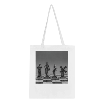 A white canvas tote bag with long shoulder straps, featuring a black and white photographic print of four chess pieces on a chessboard. The bag is shown against a plain white background.