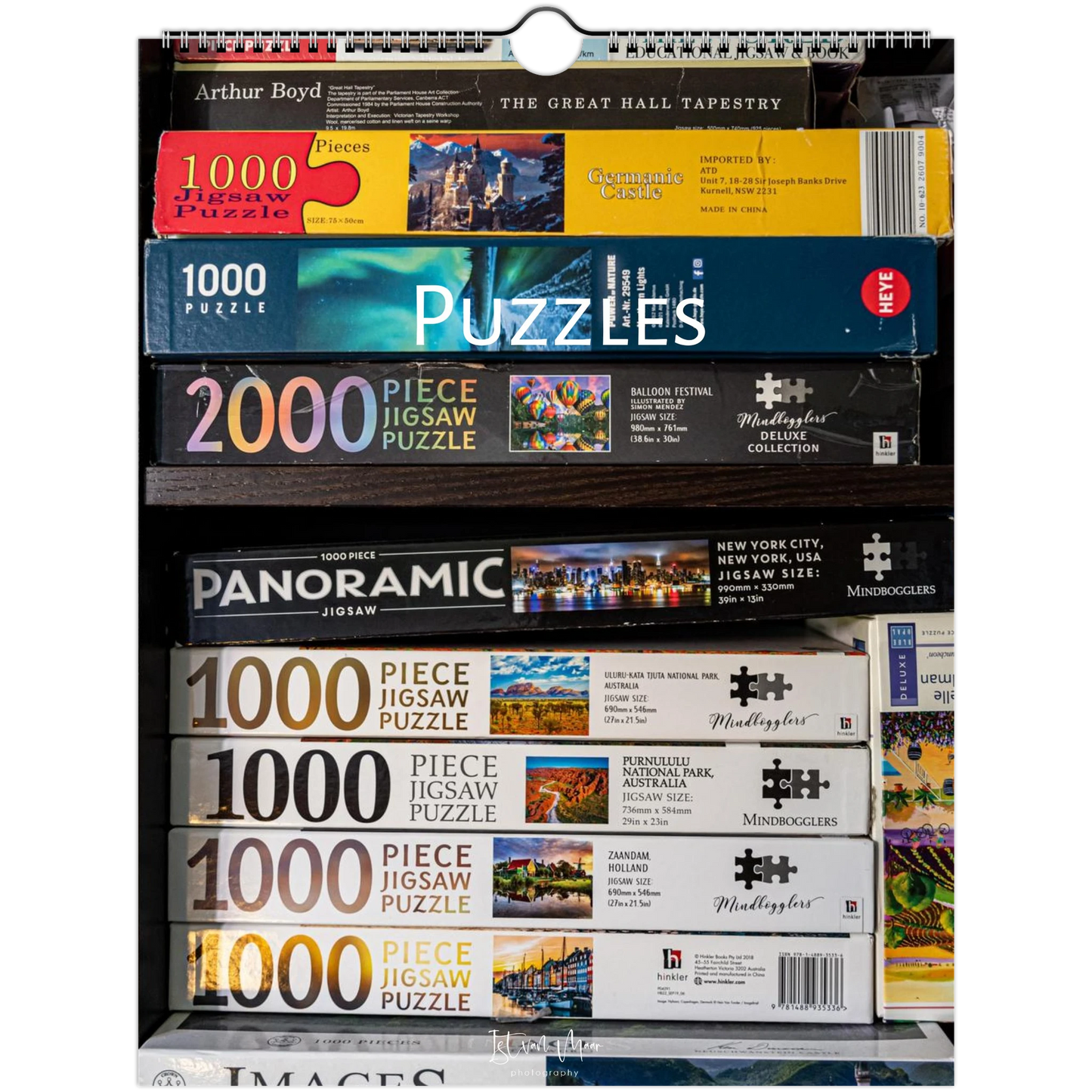 A retail display shelf filled with boxed jigsaw puzzles from multiple brands, including Arthur Boyd, Mindboggle, and Monopoly. The boxes are stacked by size, with 1000-piece and 2000-piece puzzles visible.
