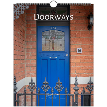 A spiral-bound wall calendar page titled 'Doorways' featuring a photograph of a bright blue front door set in a red brick wall, with decorative iron railings and the house number 374.