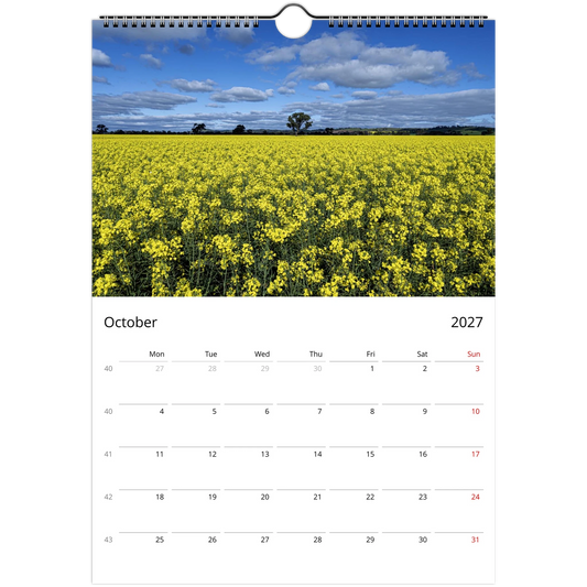 A spiral-bound wall calendar page showing a photograph of a bright yellow flower field under a blue sky with clouds, with the calendar grid for October 2027 below.