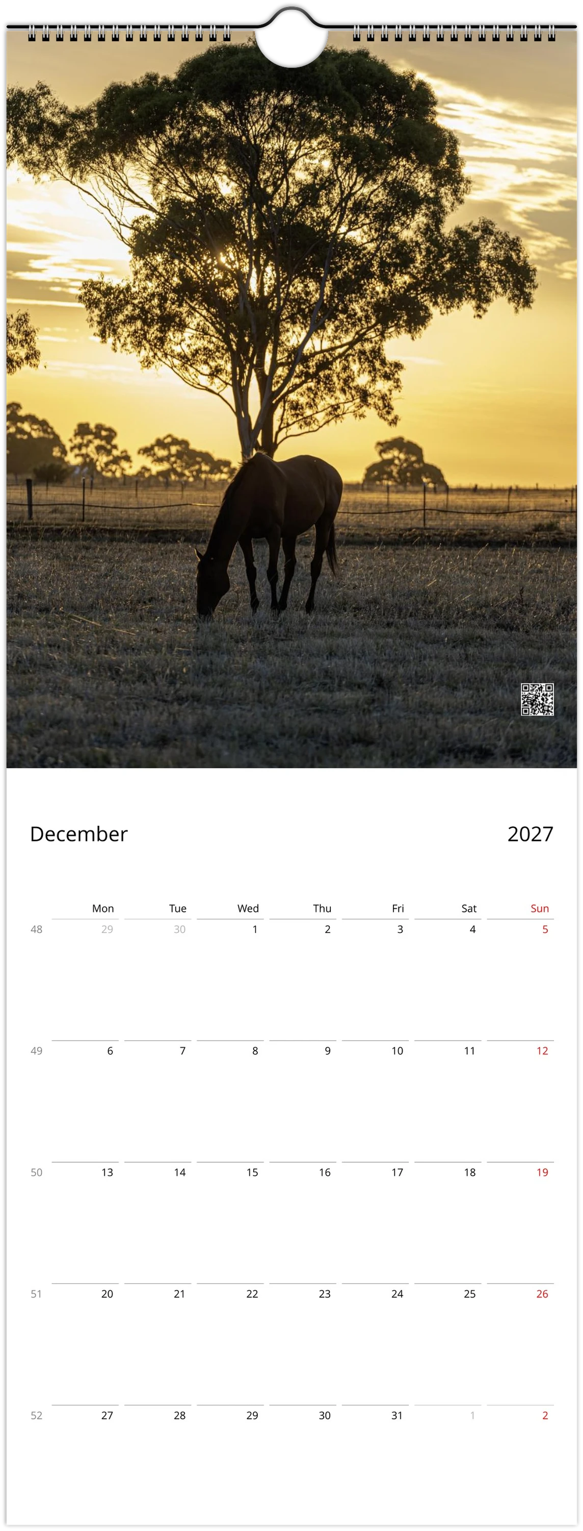 A single-page wall calendar spread showing a scenic photograph of a horse grazing under a large tree at sunset, with the calendar grid for December 2027 below on a white page.