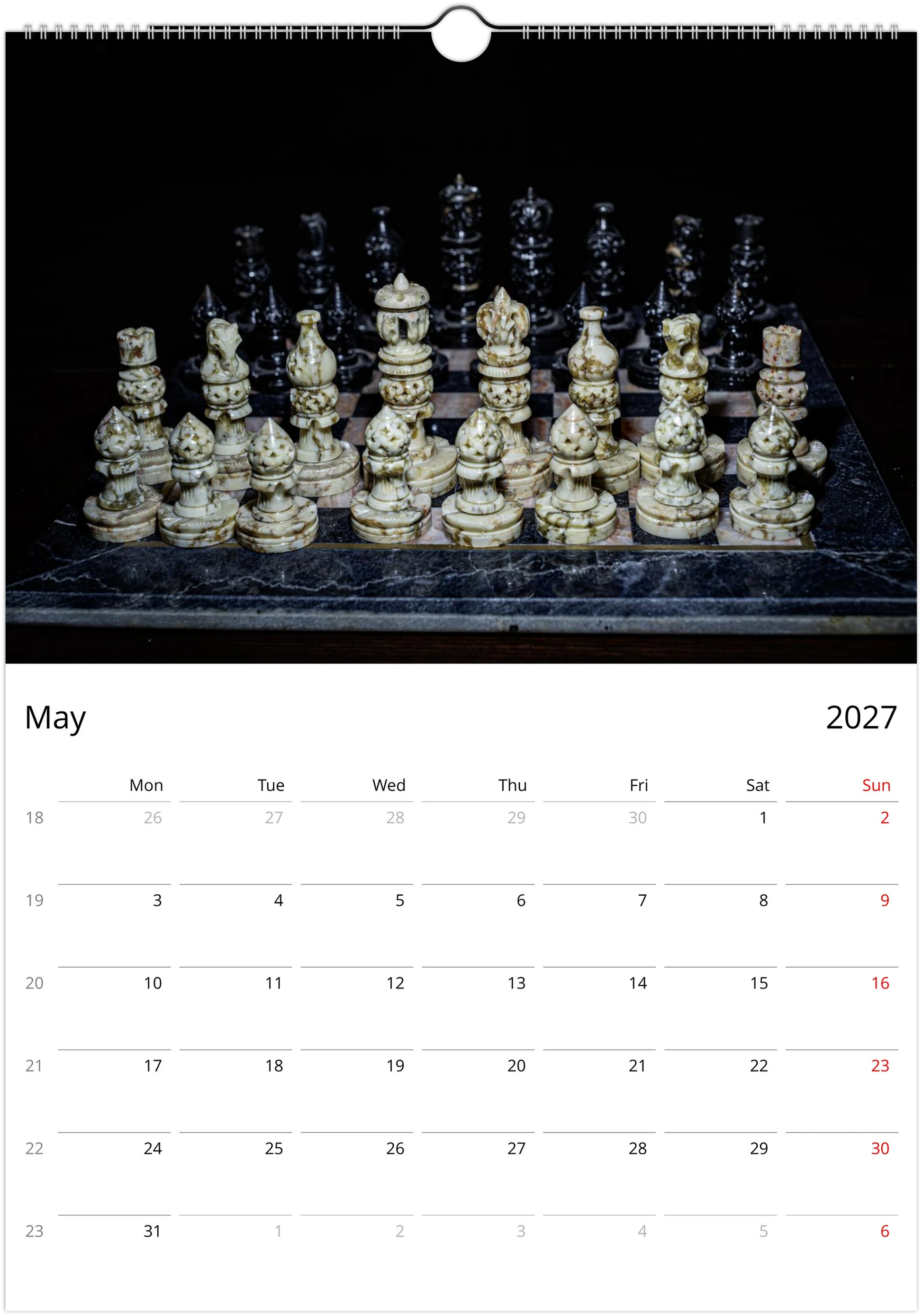 A wall calendar page for May 2027, featuring a large photograph of an ornate chess set on a dark marble board against a black background. The bottom section contains a white calendar grid with days of the week and dates in red and black text.