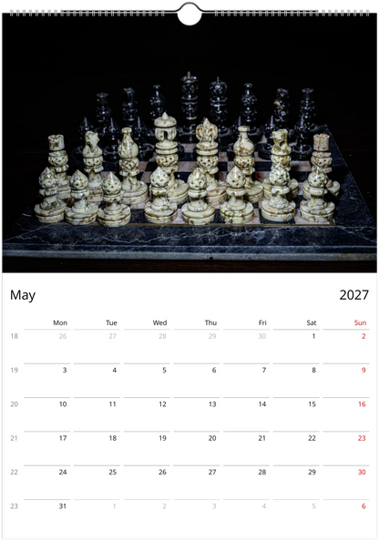 A wall calendar page for May 2027, featuring a large photograph of an ornate chess set on a dark marble board against a black background. The bottom section contains a white calendar grid with days of the week and dates in red and black text.