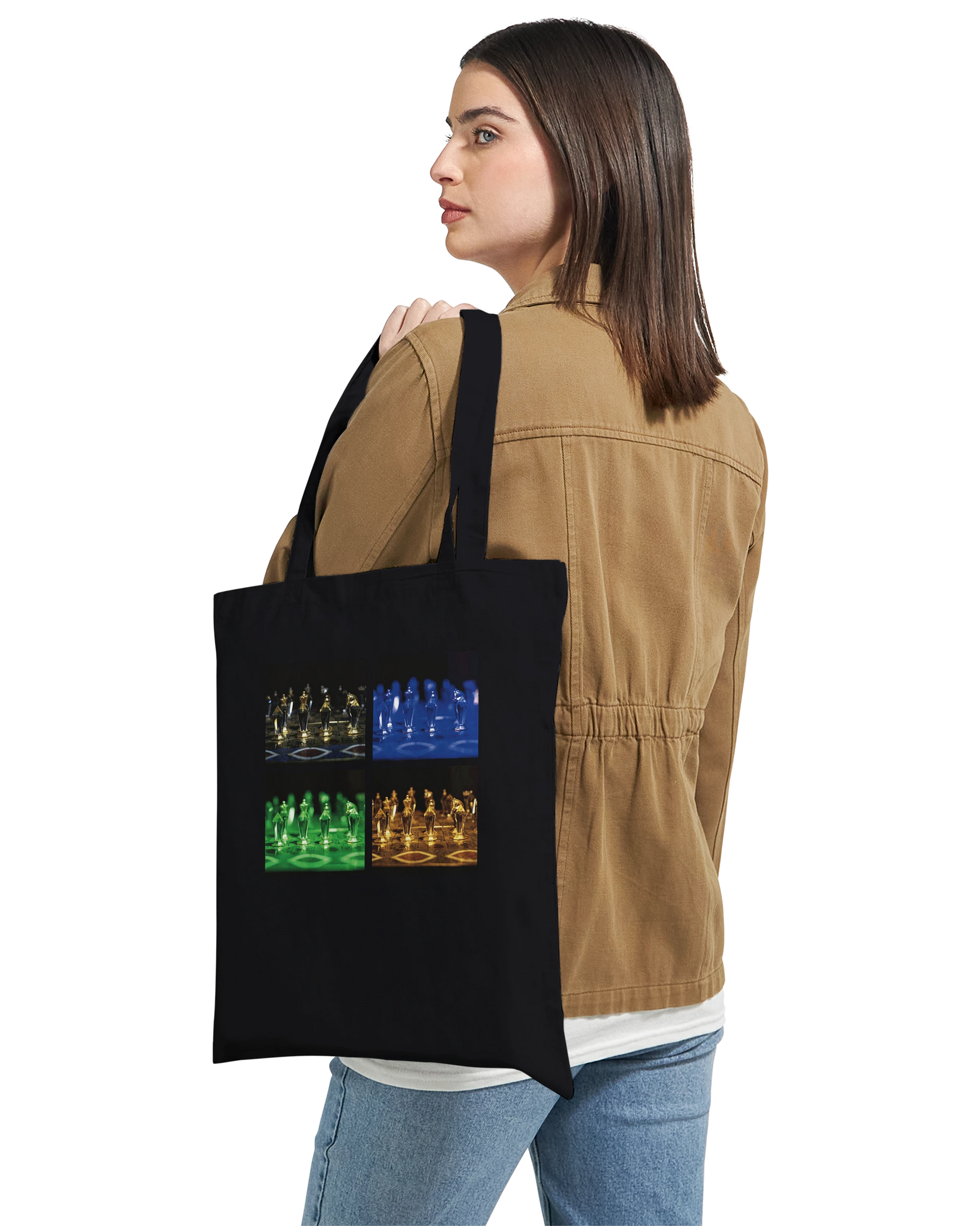A woman wearing a tan jacket and blue jeans carries a black canvas tote bag over her shoulder. The bag features a graphic print of four chess-themed panels in blue, green, and orange.