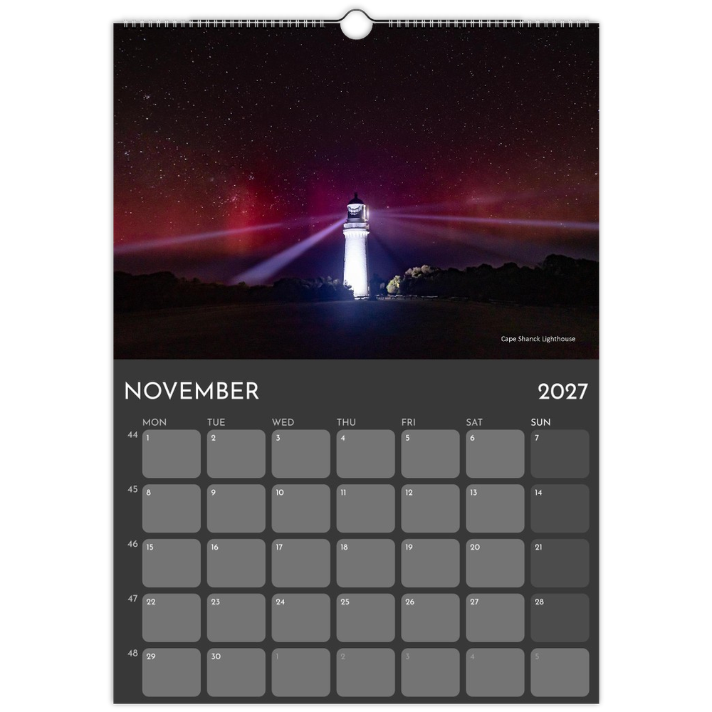 A hanging wall calendar page for November 2027, featuring a night sky lighthouse photograph at the top and a gray monthly calendar grid below.
