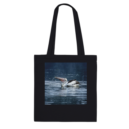 Black canvas tote bag printed with a splashing pelican photo, front view