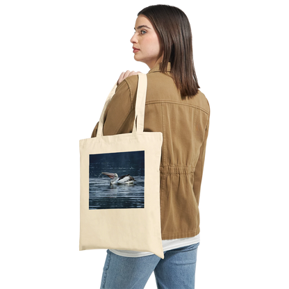 Woman carrying a natural canvas tote bag with a splashing pelican print over her shoulder