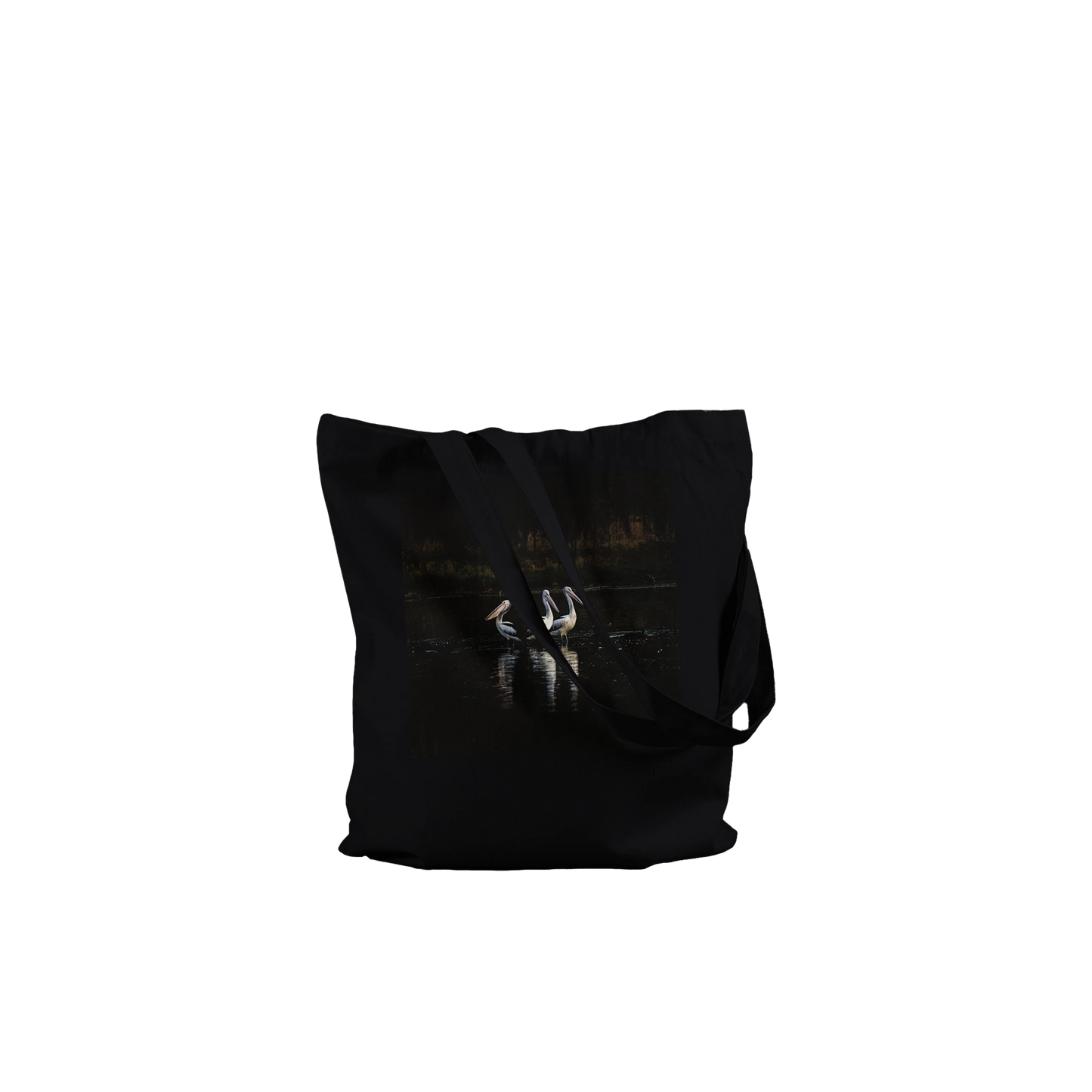 Three Pelicans canvas tote bag, black, front view laid flat with straps draped — fine art photograph of three pelicans standing together in still water at dusk