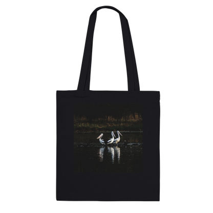 Three Pelicans canvas tote bag, black, hanging front view — fine art photograph of three pelicans standing together in still water at dusk