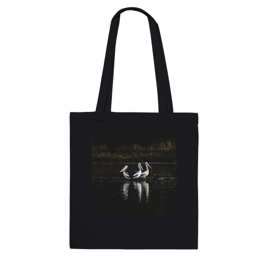 Three Pelicans canvas tote bag, black, hanging front view — fine art photograph of three pelicans standing together in still water at dusk