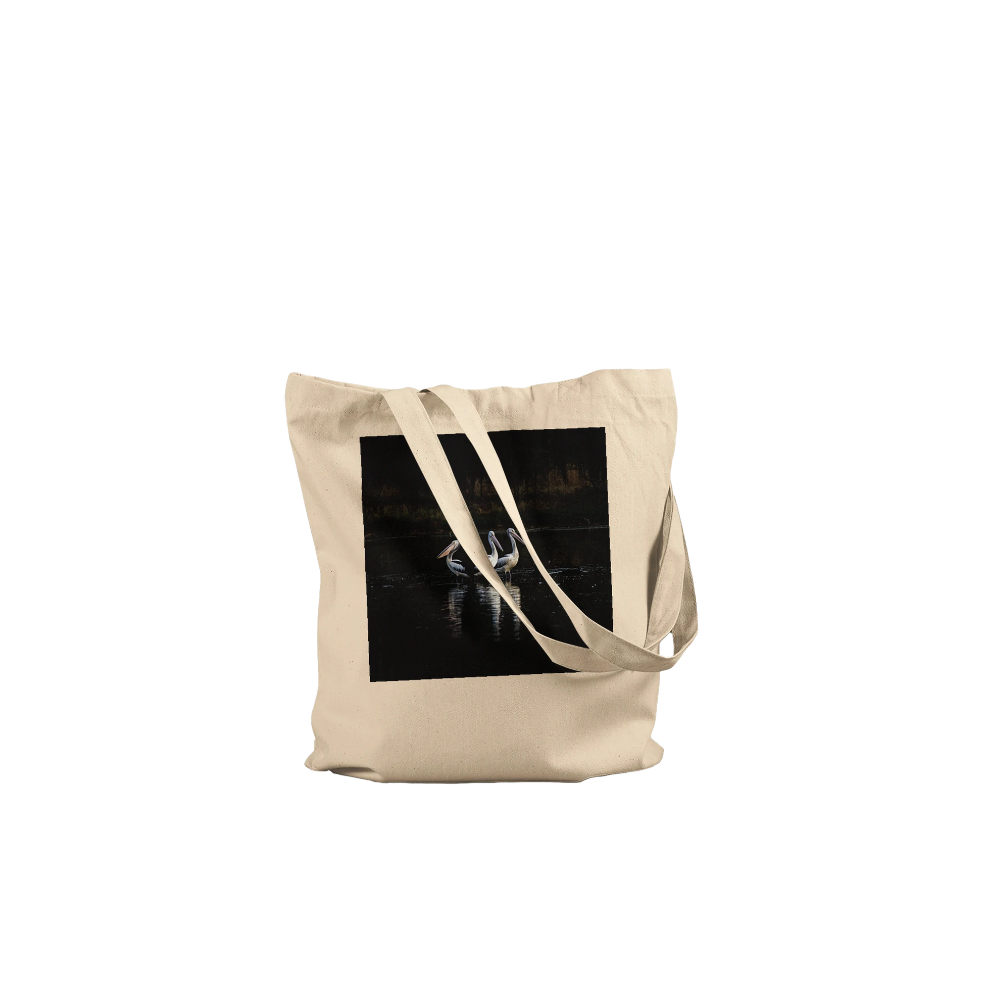Three Pelicans canvas tote bag, natural, front view laid flat with straps draped — fine art photograph of three pelicans standing together in still water at dusk