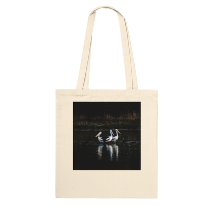 Three Pelicans canvas tote bag, natural, hanging front view close-up — fine art photograph of three pelicans standing together in still water at dusk