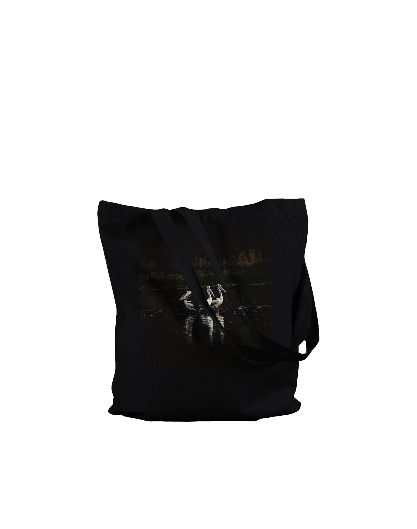 Three Pelicans canvas tote bag, Premium Black, on-ground front view — fine art photograph of three pelicans standing together in still water at dusk