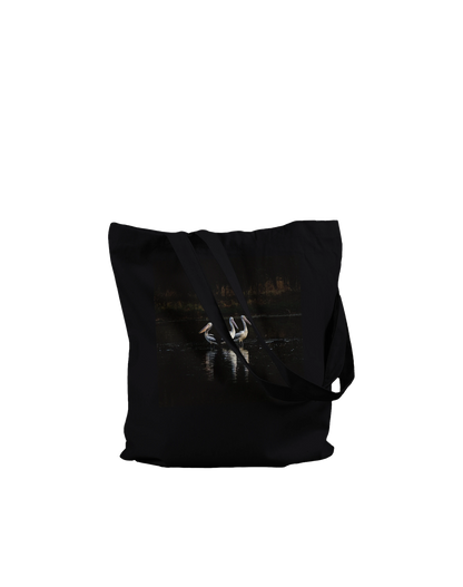 Three Pelicans canvas tote bag, Premium Black, on-ground front view — fine art photograph of three pelicans standing together in still water at dusk