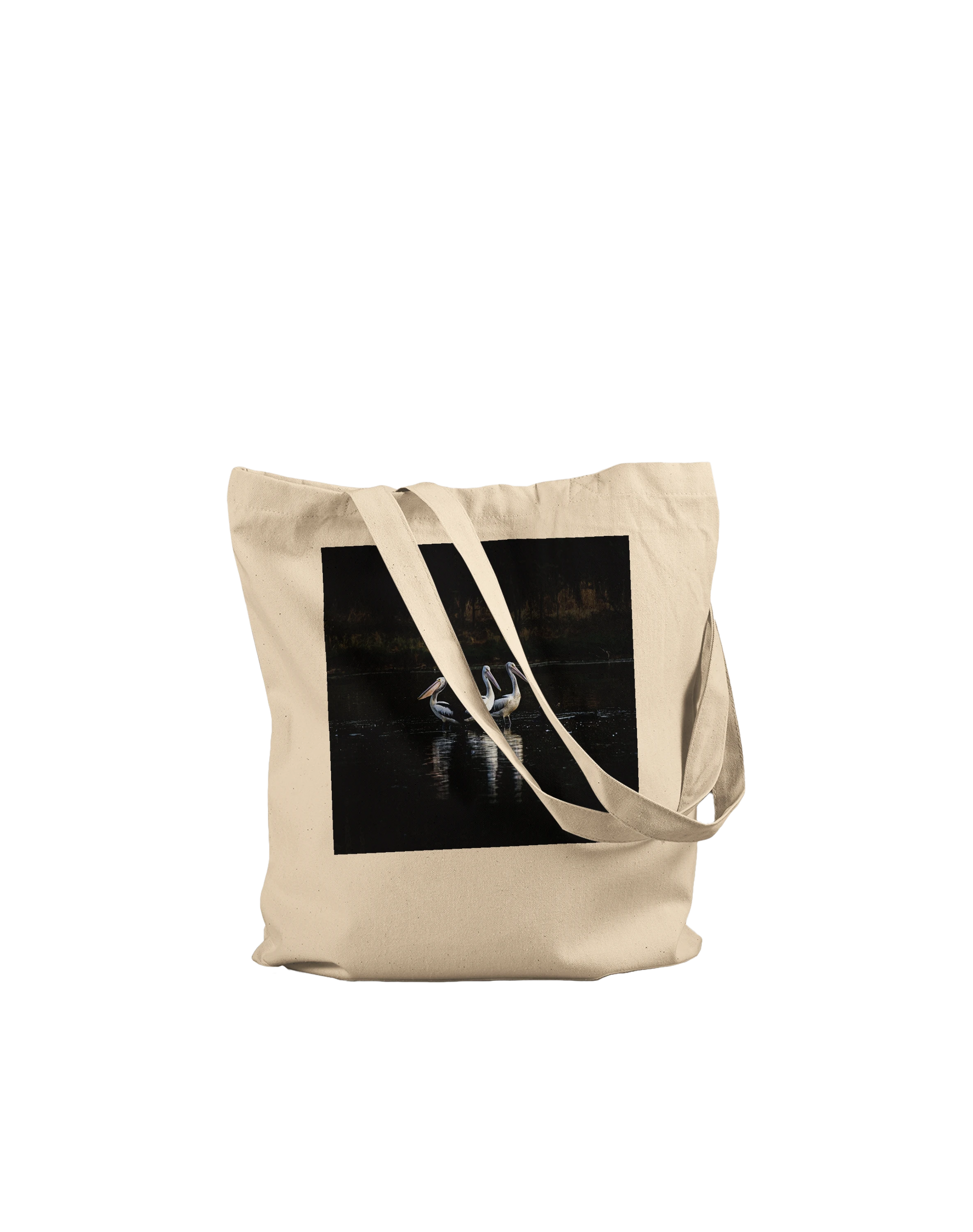 Three Pelicans canvas tote bag, Premium Natural, on-ground front view — fine art photograph of three pelicans standing together in still water at dusk